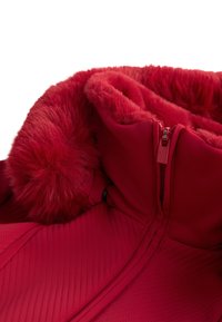 Piros dzseki műszőrme kapucni béléssel, steppelt textúrával és cipzáras záródással. Az anyag sima, elegáns kialakítású.