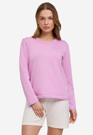 Pull à manches longues, col ras du cou en tissu rose doux associé à un short blanc texturé, avec des rayures verticales et une coupe décontractée.