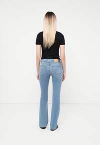 Light blue flared jeans with a faded texture, featuring a brown leather patch at the waistband and a fitted black t-shirt.