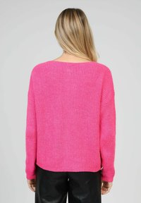 Pull surdimensionné en tricot rose avec une texture travaillée, épaules tombantes et un col large. Matière douce et confortable avec une coupe décontractée.