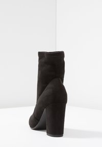 Botte de cheville en suede noir avec un haut talon bloc et un dessus sans couture, présentant une pointe arrondie et une texture lisse.