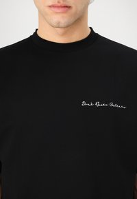 Black short-sleeve t-shirt made from cotton with a round neckline. Features embroidered white text "Don't Waste Colors" on the front.