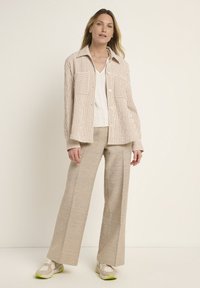 Striped beige and cream button-up shirt with two chest pockets, paired with light beige wide-leg pants and beige sneakers with green accents.