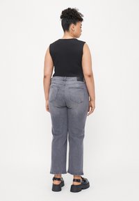 Czarny top bez rękawów zestawiony z wysokimi, szarymi dżinsami. Stylizacja dopełniona chunky czarnymi sandałami. Prosty, nowoczesny design.