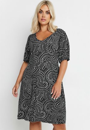 Sort kjole med V-hals, korte ærmer og en flagrende design, der har et hvidt blomstermønster og svungne former på stoffet.