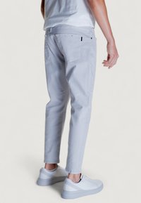 Jeans de algodón gris claro con un corte ajustado, que presentan bolsillos traseros y una sutil etiqueta negra, combinados con zapatillas blancas.