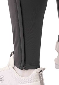 Donkergrijze sportbroeken gemaakt van rekbaar materiaal, met een ritssluiting bij de enkel en gecombineerd met witte sneakers. Zachte textuur en aansluitend ontwerp.