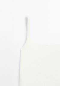 Weißes gestricktes Oberteil mit dünnen Trägern, quadratischem Ausschnitt und weicher Textur. Das Design ist minimalistisch und figurbetont.