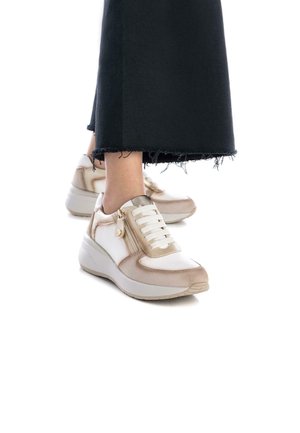 Zapatillas con un diseño ligero, que presentan un esquema de color crema y beige, detalle de cremallera y acentos texturizados, combinadas con pantalones negros cortos.