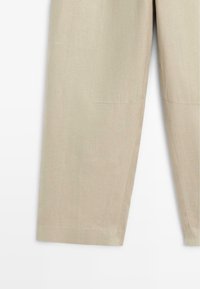 Pantalons beige à jambes droites en tissu texturé, montrant la moitié inférieure avec des détails de coutures visibles et des bords d'ourlet nets.