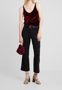 Top in velluto bordeaux, pantaloni neri su misura, tacchi verdi con cinturino e una piccola borsa bordeaux. Cintura nera con fibbia rotonda.
