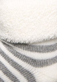 Calcetines rayados en blanco y gris con una textura de felpa, que cuentan con un diseño de punto suave y un borde superior redondeado para mayor comodidad.