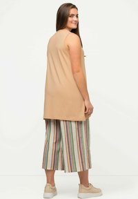 Top senza maniche beige abbinato a pantaloni larghi a righe con strisce verdi, viola e gialle. Sneakers bianche completano l'outfit.