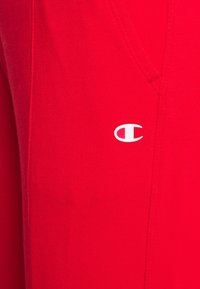 Röda bomullsbyxor med en liten vit logotyp på vänster sida. Inkluderar sidofickor och har en mjuk textur.