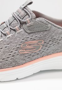 Grå nät sneakers med en strukturerad yta, rosa detaljer och en vit sula. Har elastiska snören och en logotyp på sidan.