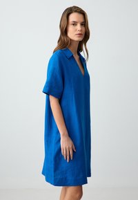 Abito a maniche corte in lino blu vivace, con scollatura a V e una vestibilità rilassata e oversize, dotato di una superficie liscia e leggermente strutturata.