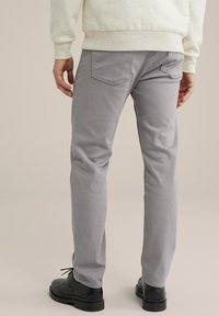Gray cotton trousers with a slim fit, featuring two back pockets and stitched detailing. Paired with black lace-up shoes.