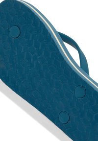 Sininen kuminen flip-flop-pohja, jossa on teksturoitu hunajakennokuvio ja kaksi pyöreää painaumaa, sekä valkoinen raita reunan ympärillä.