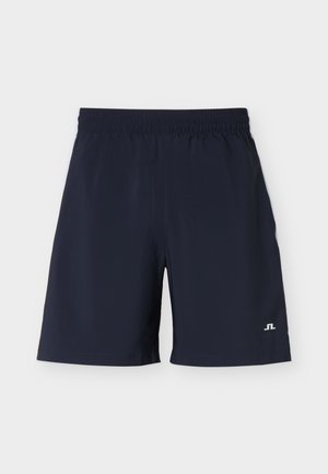 Tumesinised meeste spordipüksid elastse vöökoha ja väikese valge logoga paremal alajäsemel tavalise tausta ees.