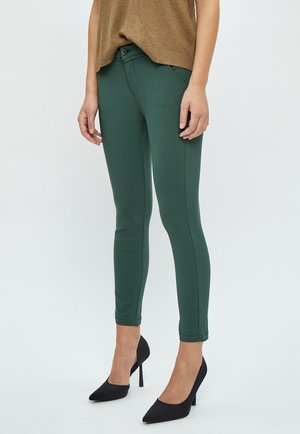 Tmavě zelené, elastické skinny džíny s klasickým designem pěti kapes, předním zapínáním na knoflík a čistým lemem. Nosit s černými vysokými podpatky.