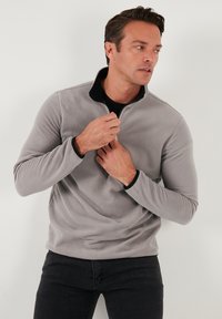 Grå fleecepullover med sort krave, kvart-zip front, tekstureret stof, lange ærmer og elastiske manchetter. Båret over en sort skjorte.