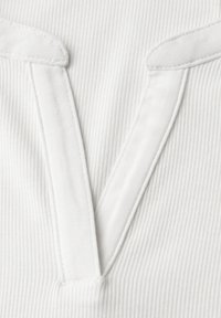 Biały prążkowany materiał z głębokim dekoltem w kształcie litery V, ozdobiony szerokim, przeszywanym obszyciem na elemencie ubrania.