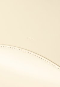 Επιφάνεια από κρεμ δέρμα με ραμμένη καμπυλωτή ραφή και ανεπαίσθητο ανάγλυφο όνομα επωνυμίας "TOSO" κοντά στο κέντρο.