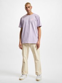Lavender cotton t-shirt with a small floral embroidery on the left chest, paired with beige rolled-up pants and white sneakers.