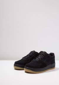 Sneaker in suede nero con design a collo basso, caratterizzate da accenti perforati, chiusura con lacci e suola in gomma marrone chiaro.