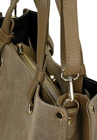 Béžová semišová kabelka s texturovaným povrchem, dvojitými uchy, zlatými kovovými prvky a kapsou na zip. Viditelná hladká vnitřní podšívka.