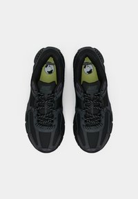 Un paio di scarpe da corsa Nike Vomero 5 nere con lacci riflettenti e solette verde lime viste dall'alto su uno sfondo bianco.