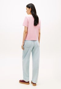 Ροζ κοντομάνικο μπλουζάκι με στρογγυλή λαιμόκοψη, συνδυασμένο με ανοιχτό μπλε τζιν παντελόνι με φαρδιά πόδια. Το τζιν έχει δύο πίσω τσέπες. Το σύνολο ολοκληρώνεται με καφέ αθλητικά παπούτσια.