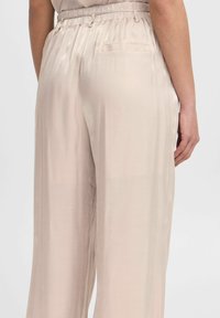 Lichtbeige satijnen broek met een gladde textuur, elastische tailleband en een enkele zak aan de rechterachterkant.