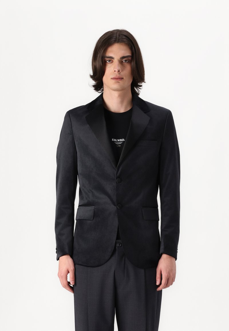 Blazer negro de tejido suave con solapas de satén, dos bolsillos frontales y cierre de un solo botón, usado sobre una camiseta negra.