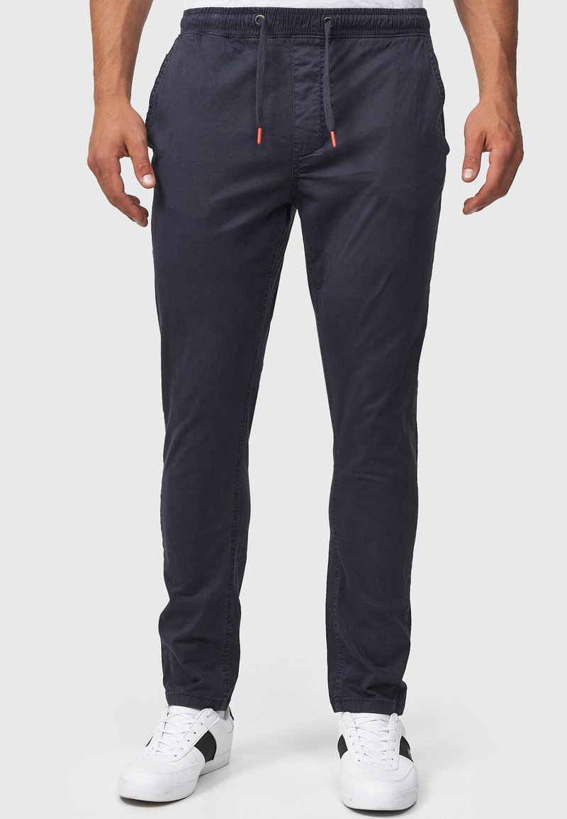 Navy blue cotton jogger pants with an elastic waistband, drawstring closure, and two side pockets, paired with white sneakers.
