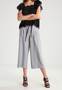 Blusa nera a maniche corte con rifiniture in pizzo abbinata a pantaloni cropped larghi grigi chiari con vita legata. Sandali neri con fascia.