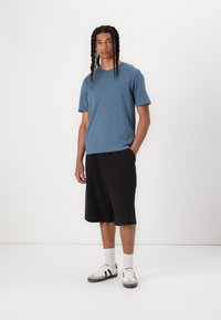 Blue short-sleeve t-shirt paired with black knee-length shorts and white sneakers with gray accents. Fabric appears smooth, casual design.