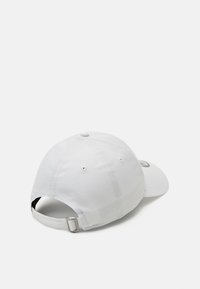 Boné de beisebol branco com uma aba curva, faixa ajustável na parte de trás e buracos de ventilação nas laterais. Textura de tecido suave.