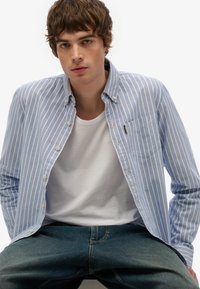Lichtblauw gestreepte button-up shirt, zachte katoenen stof, standaard kraag, enkel borstzakje, gelaagd over een wit crew-neck t-shirt.