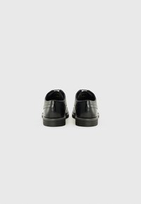 Zapatos de cuero negro con un acabado suave, punta redondeada y tacón bajo. Presentan costuras mínimas y dos lengüetas en la parte posterior para facilitar su uso.