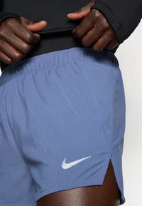 Απαλά μπλε αθλητικά σορτς με διάτρητο σχέδιο, ελαστική μέση και λευκό λογότυπο Nike στην κάτω αριστερή πλευρά.