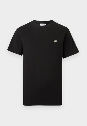 Mustast lühikeste varrukatega ümara kaelusega T-särk, mille vasakul rinnal on väike roheline krokodillilogo ja vasakul varrukal logo triip.