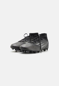 Black football boots with a knitted top, featuring a textured surface, gray striping, and black studs for traction. Laces partially undone.
