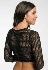 Schwarzes Spitzen-Crop-Top mit Karomuster, langen Ärmeln und gewelltem Saum. Das semi-transparente Material betont die Textur und Details.