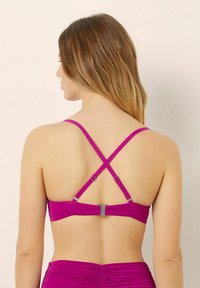 Top bikini fucsia con spalline incrociate regolabili, clasp metallico sul retro e texture liscia.
