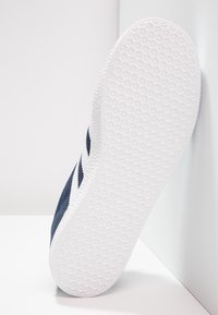 Navy blue sneaker with a textured white rubber sole. Features a smooth canvas upper and a contrasting design element on the side.