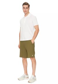 Witte polo met korte mouwen, olijfgroene shorts en lichtgrijze sneakers. De shorts hebben zijzakken en een klein logo-detail.