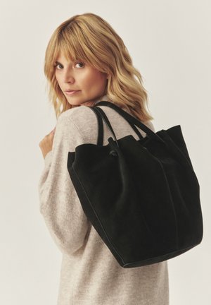 Black suede tote bag with a rounded top, featuring two sturdy handles and a smooth, matte texture. Shallow pleats detail the sides.