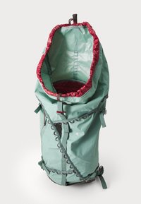 Sac à dos en tissu vert avec un intérieur rouge profond, cordon de serrage en haut, bretelles réglables et détails de couture complexes à l'extérieur.