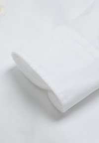 Manga de camisa de algodón blanca con una textura suave, que presenta un puño vuelto y costuras limpias. Diseño sencillo, sin patrones ni adornos.